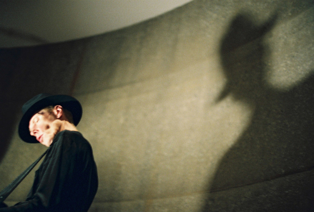 Jandek wearing a hat casting a Nosferatu vibe shadow on a curved wall