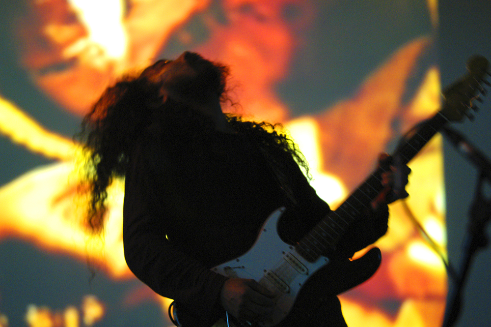 Makoto Kawabata playing electric guitar in front of a projection 