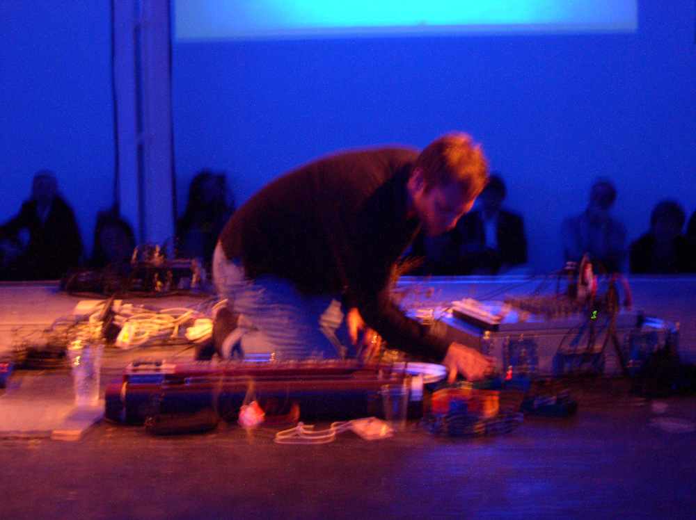 Steve Roden kneeling near musical equipment in blue light