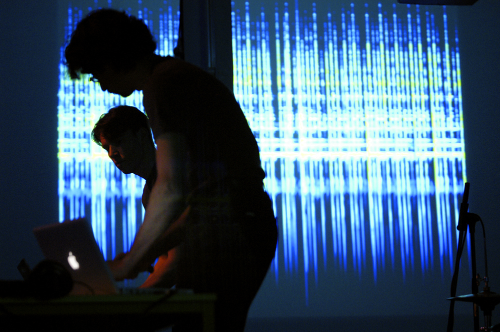 Two performers silhouetted against a projection of blue light