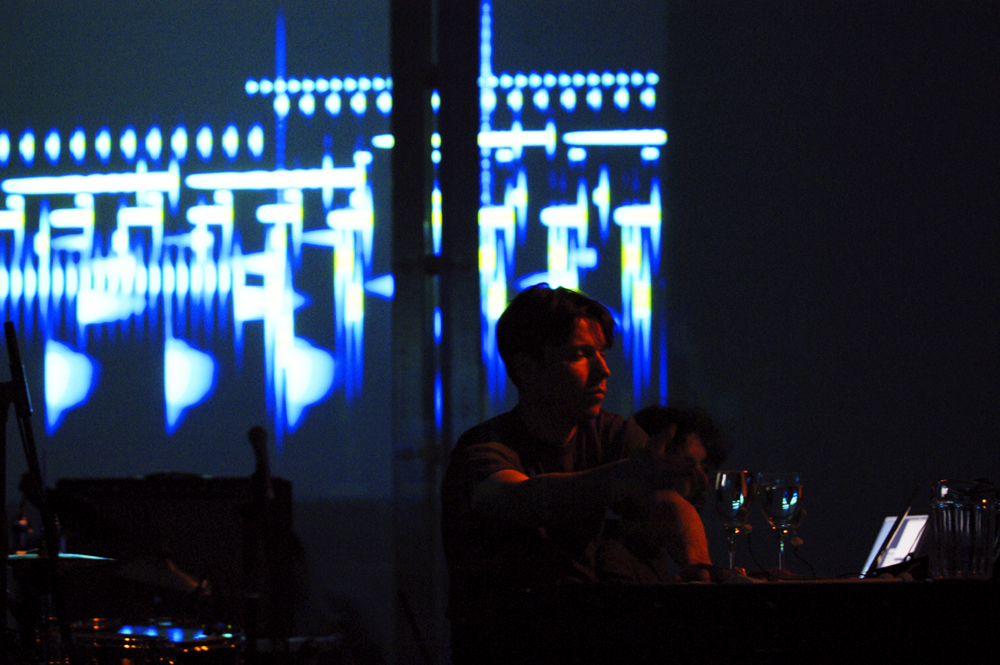 A man seated at a table in front of a screen of projections