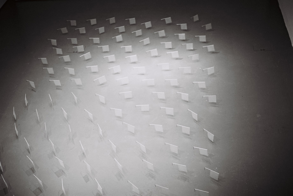 Lots of tiny paper and wire sails arranged on a grey floor 