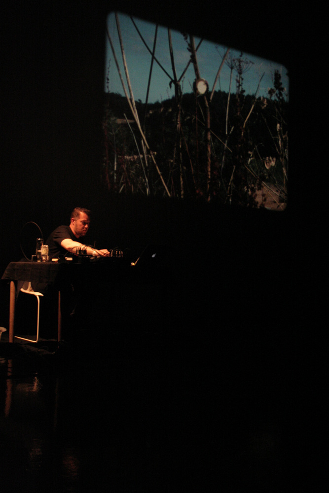 Lee Patterson sitting next to a projection of a contact mic on a bush