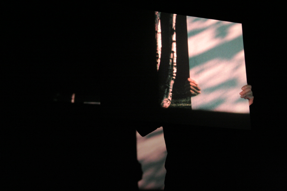 Guy sherwin holding a mirror showing a projection of himself with another mirror