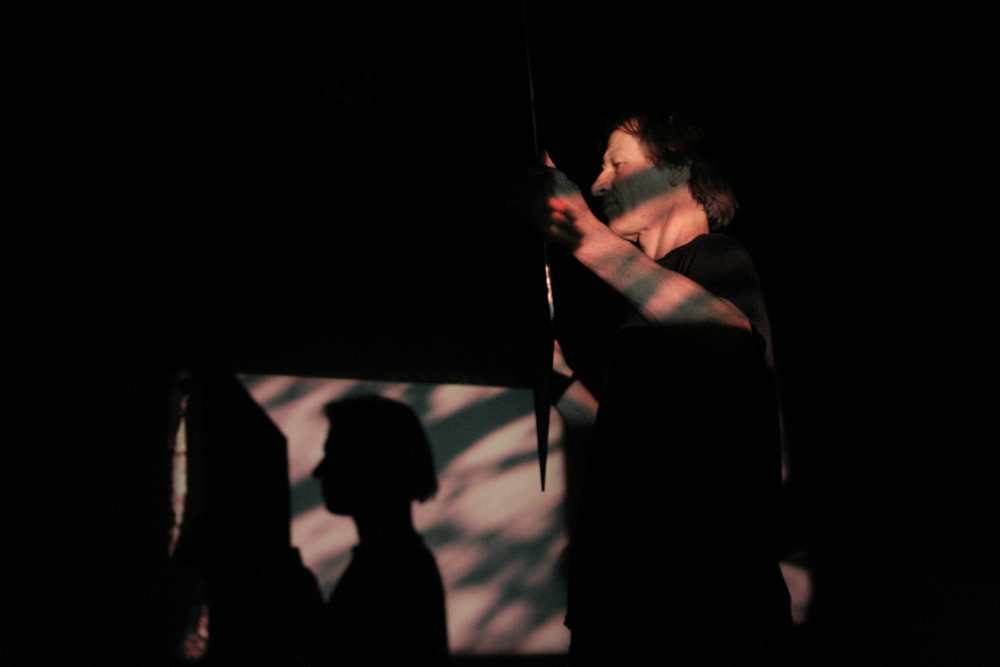 Guy Sherwin holding a mirror in profile, a shadow behind him