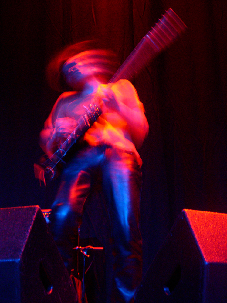 A guitarist blurred in movement and pink light performing at MLFC 05