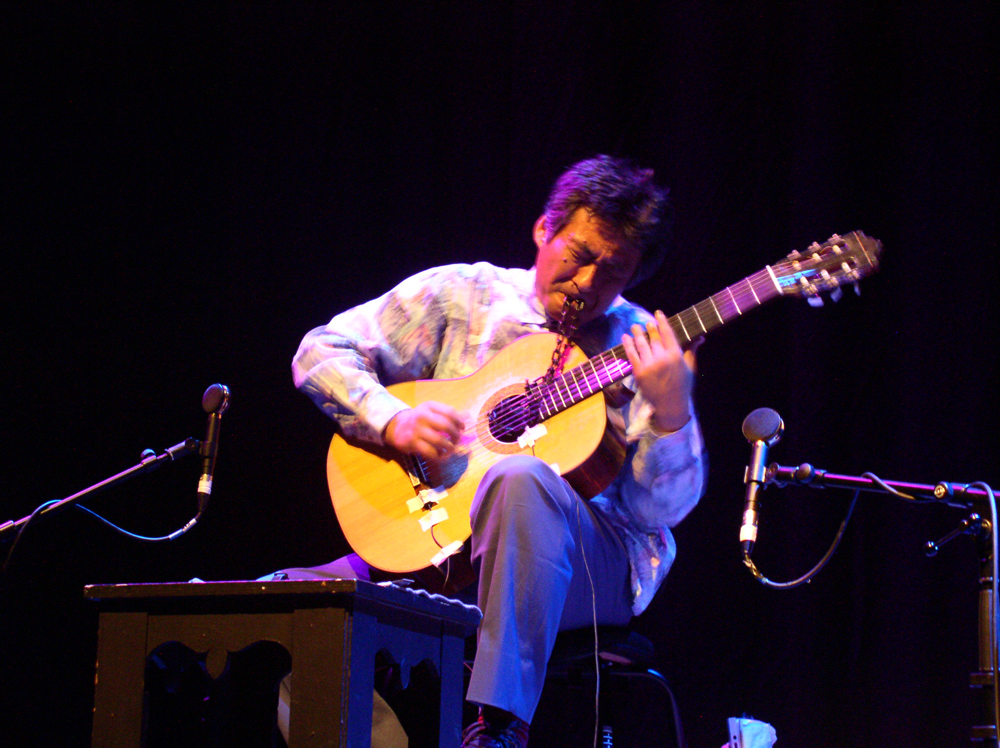 Kazuo Imai playing an acoustic guitar on stage at MLFC 05