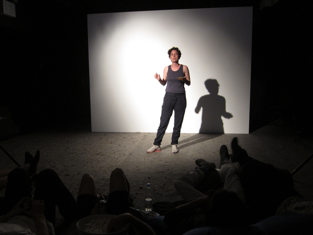 A person stands in a spotlight and talks to an audience