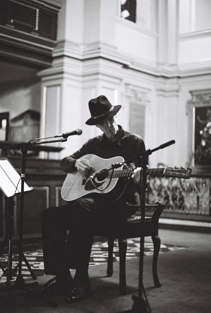 Jandek playing an acoustic guitar and wearing a hat
