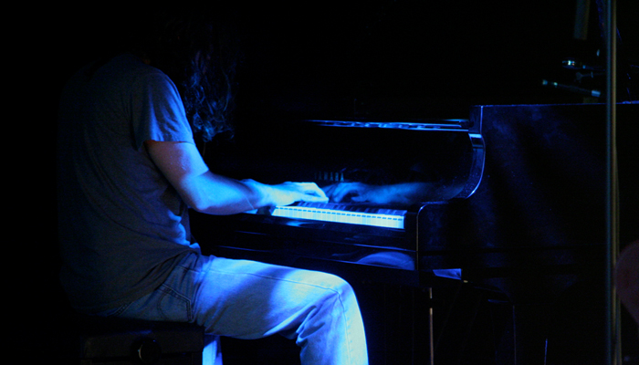 John Blum seated at a piano in blue light at MLFC 07