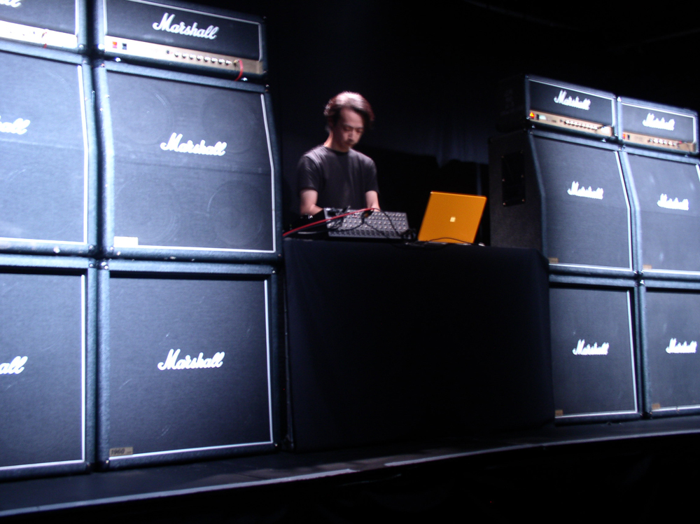 Rioji Ikeda operating a laptop surrounded by Marshall amplifiers