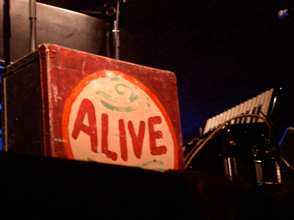 A packing case with the word ALIVE painted on it sits on stage