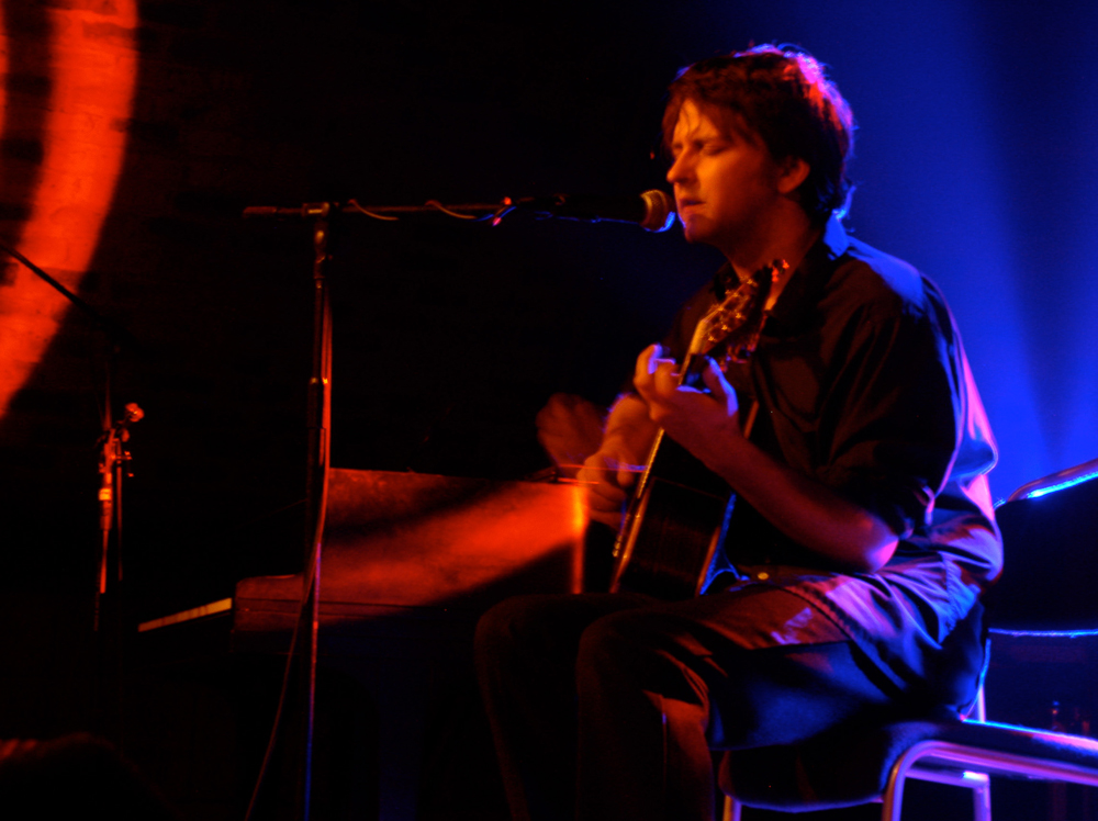Ben Chasney playing an acoustic guitar in red and blue light