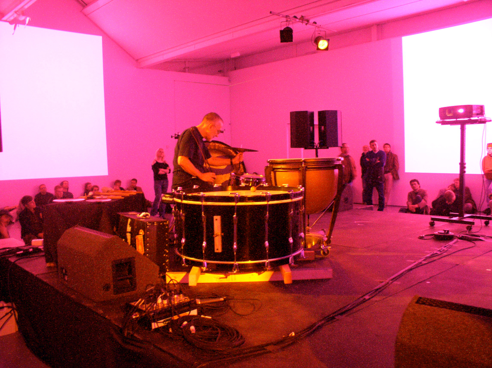 Eddie Prevost playing a large horizontal bass drum in pink light