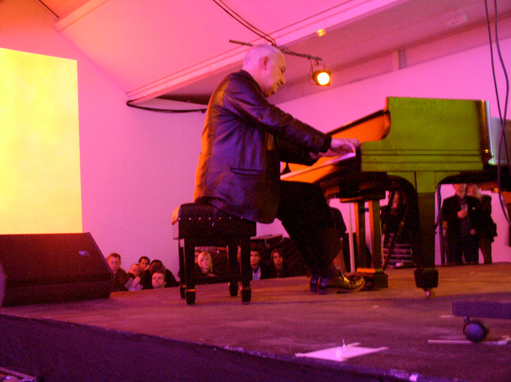 John Tilbury playing a piano in a room full of pink light