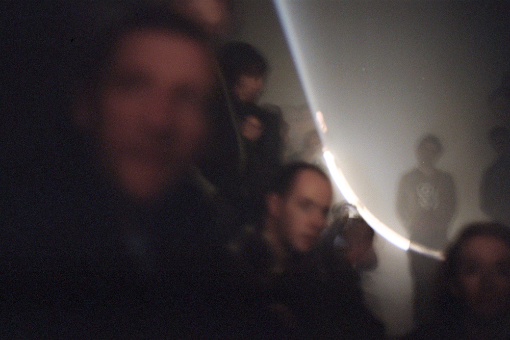 A cross section of a cone of light seen above an audience in darkness