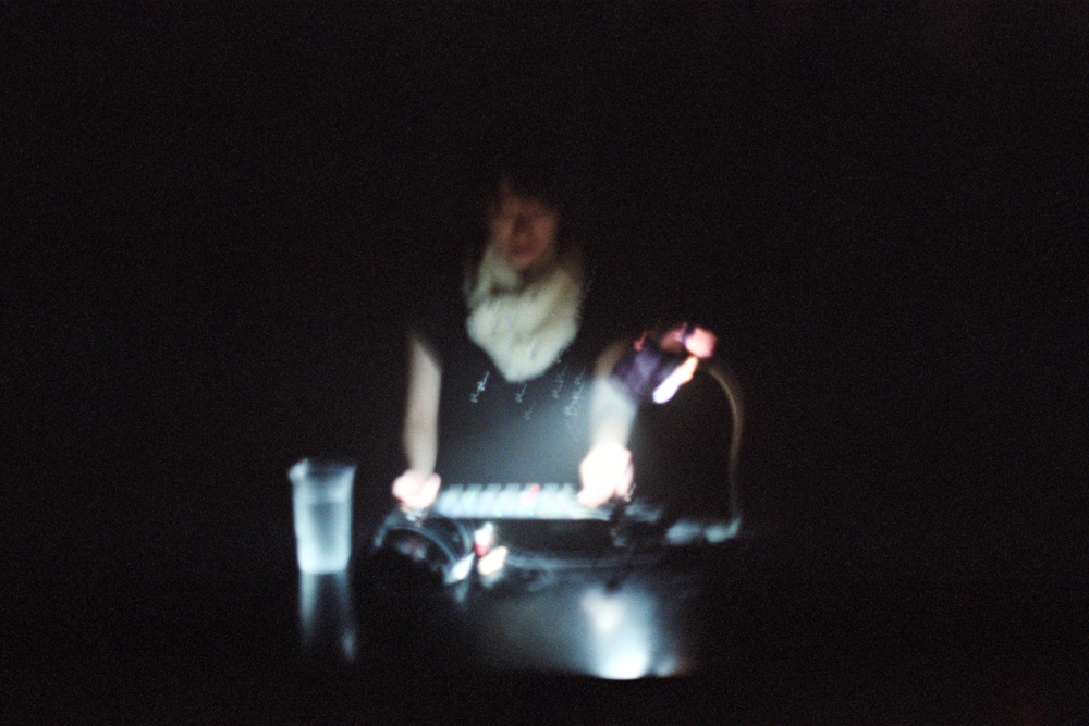 Sachiko M wearing a white scarf near some music equipment