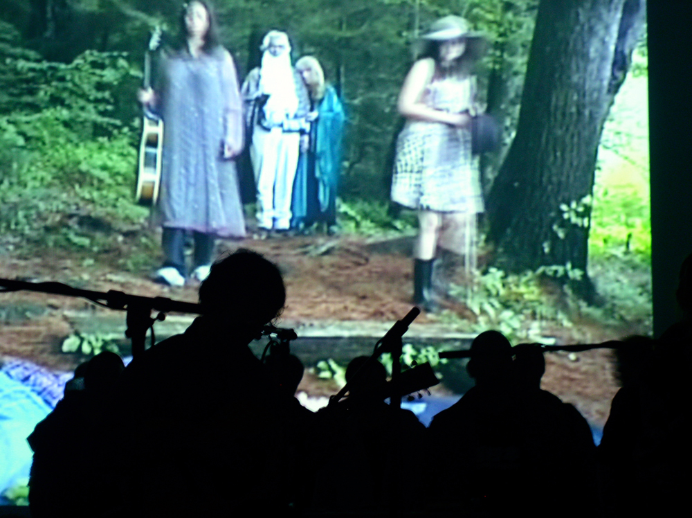 Heads of musicians silhouetted against a film projected on a wall 