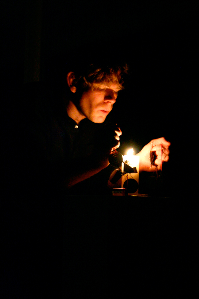 Joe Colley's face lit by a candle his hand holding an electrode nearby