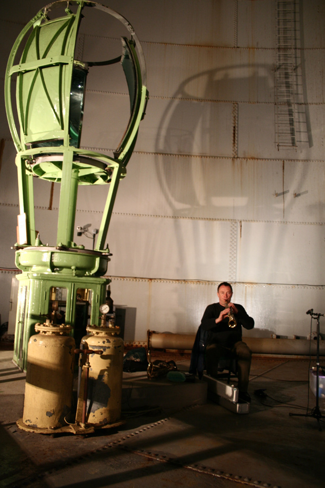 John Butcher playing soprano sax in an oil tank next to old metal machinery
