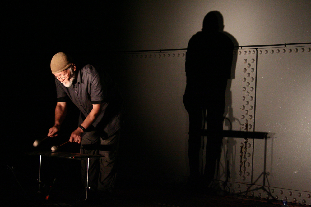 Akio Suzuki playing a percussion instrument inside an oil tank