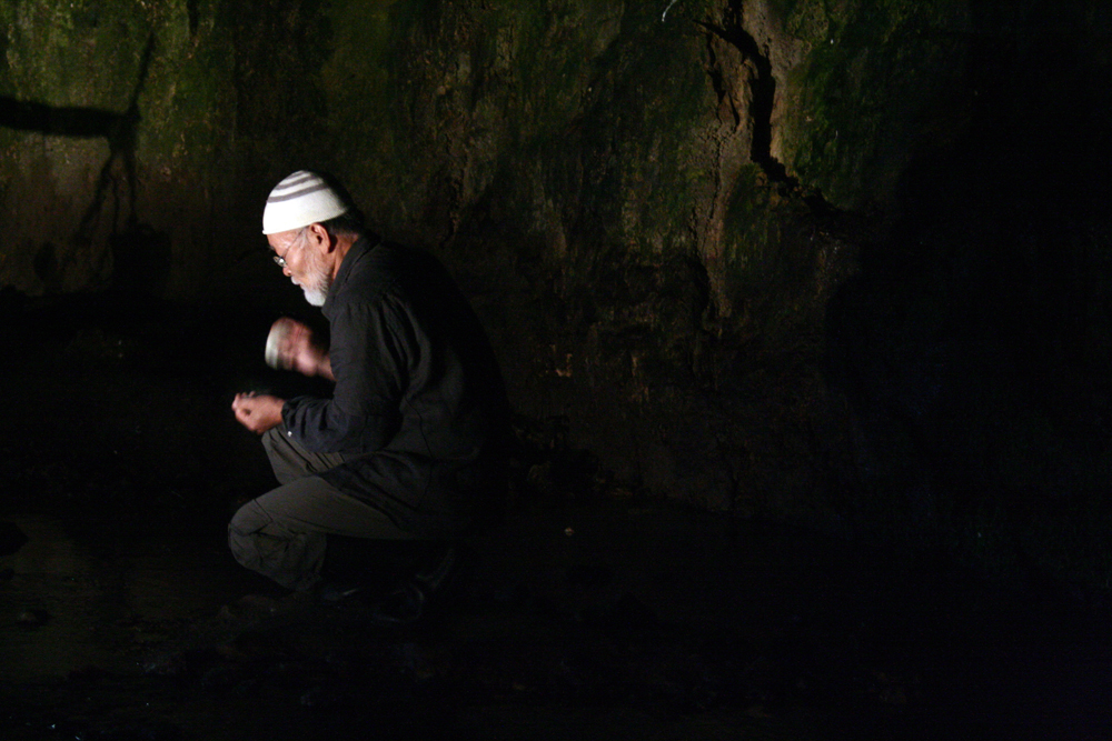 Akio Suzuki tapping stones together in the entrance to a cave