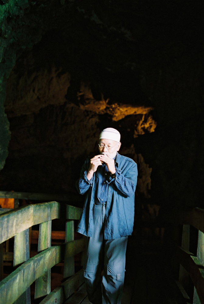 Akio Suzuki blowing a small object on a bridge in a cave