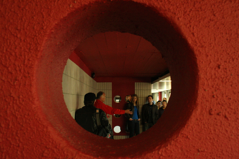 Denis Wood talking to an audience seen through the aperture of an orange hole