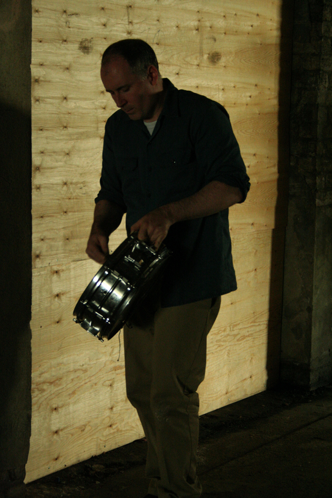 Sean Meehan carrying a snare drum through an underpass lined with plywood