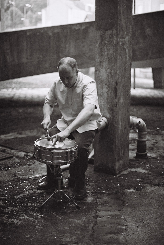 Sean Meehan playing a snare near concrete forms in Dundee