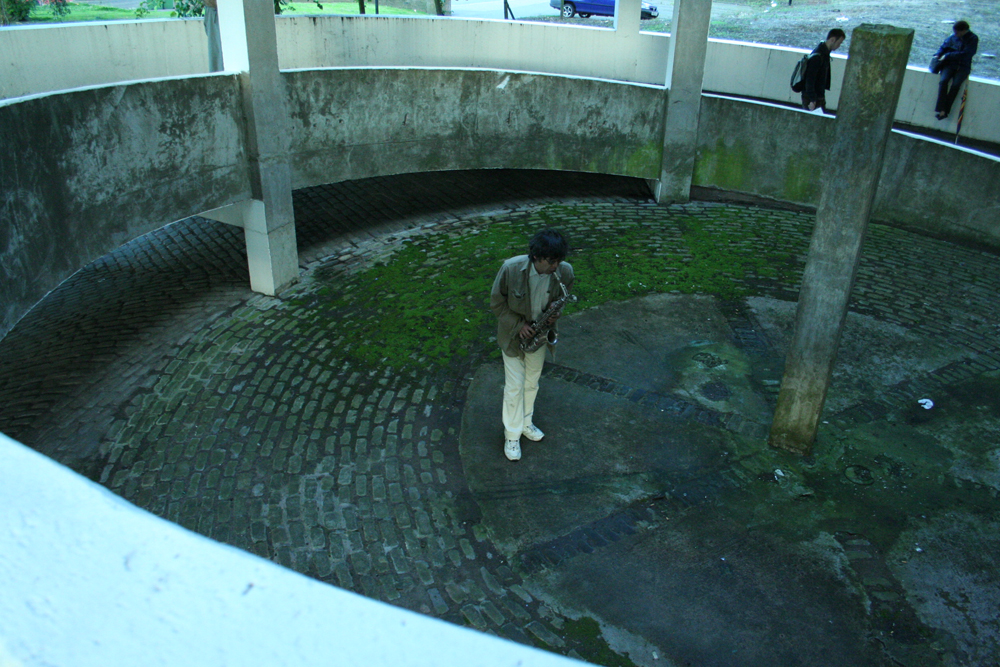 Tamio Shiraishi playing saxophone in a concrete spiral: white jeans white shoes