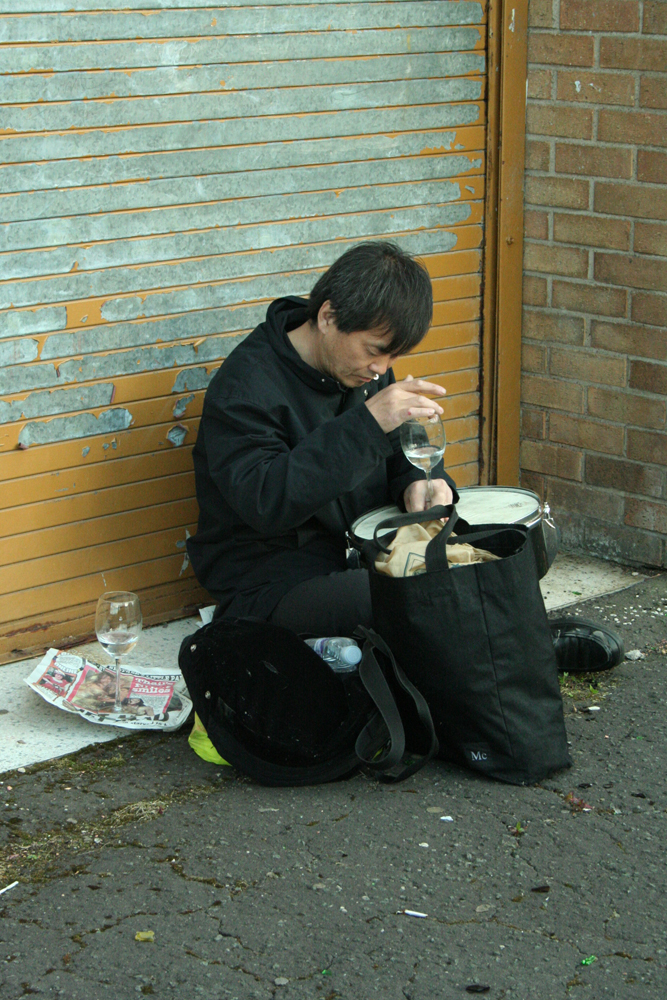 Ikuru Takehashi playing a snare with a wine glass and water near a metal door