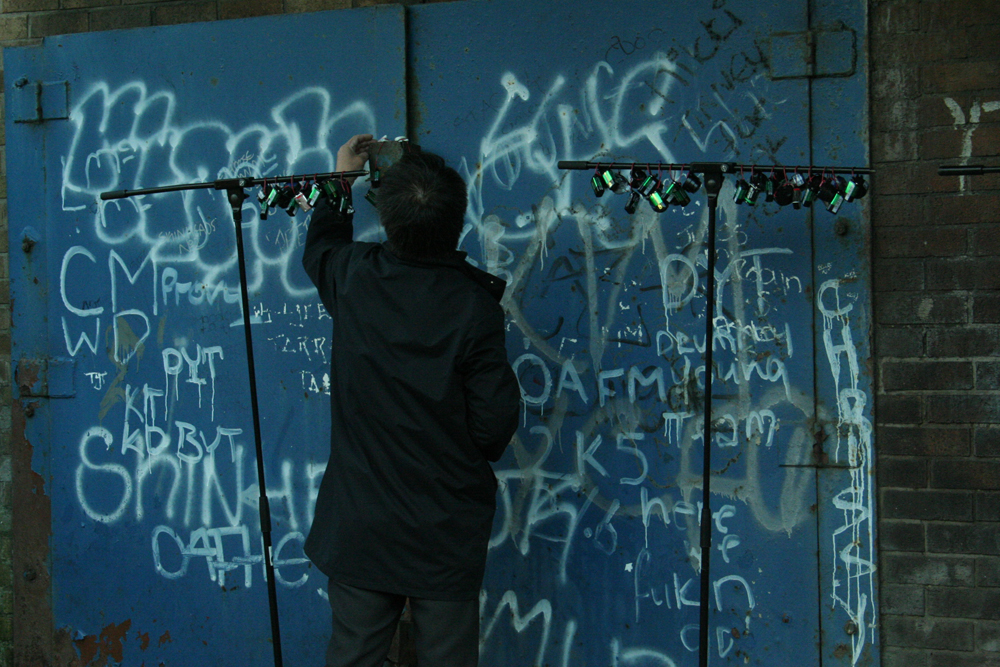 Ikuru Takehashi hanging devices on mic stands near graffitied doors