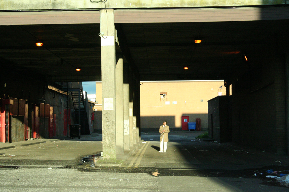 Tamio with saxophone dwarfed by concrete structures and sunset