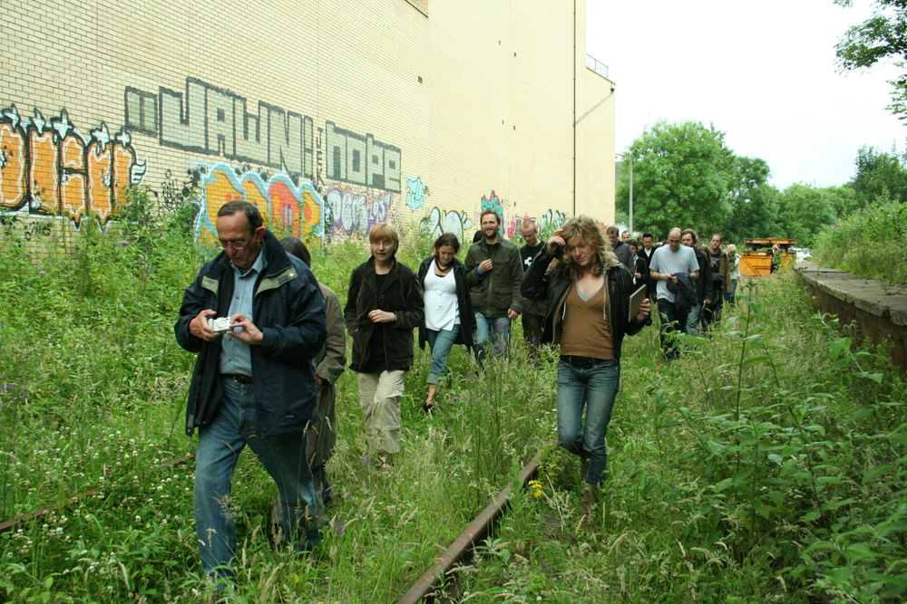 An audience walking along an abandoned railway line: graffiti and plants
