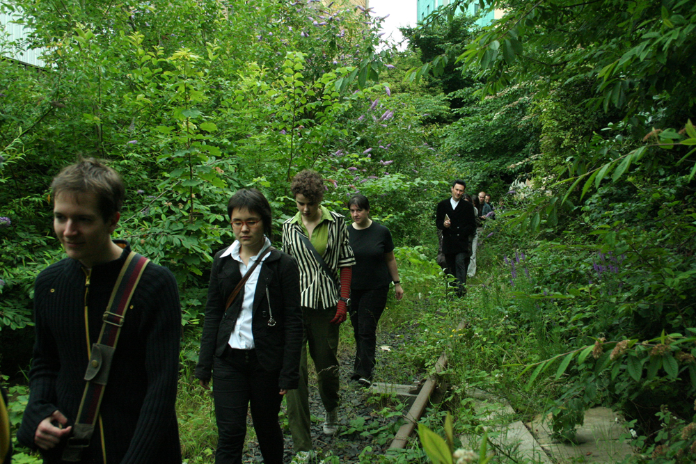 Audience members walking along a railway lined with trees and flowers