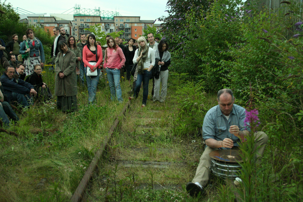 An audience watching Sean Meehan play a cymbal on a railway track in Edinburgh