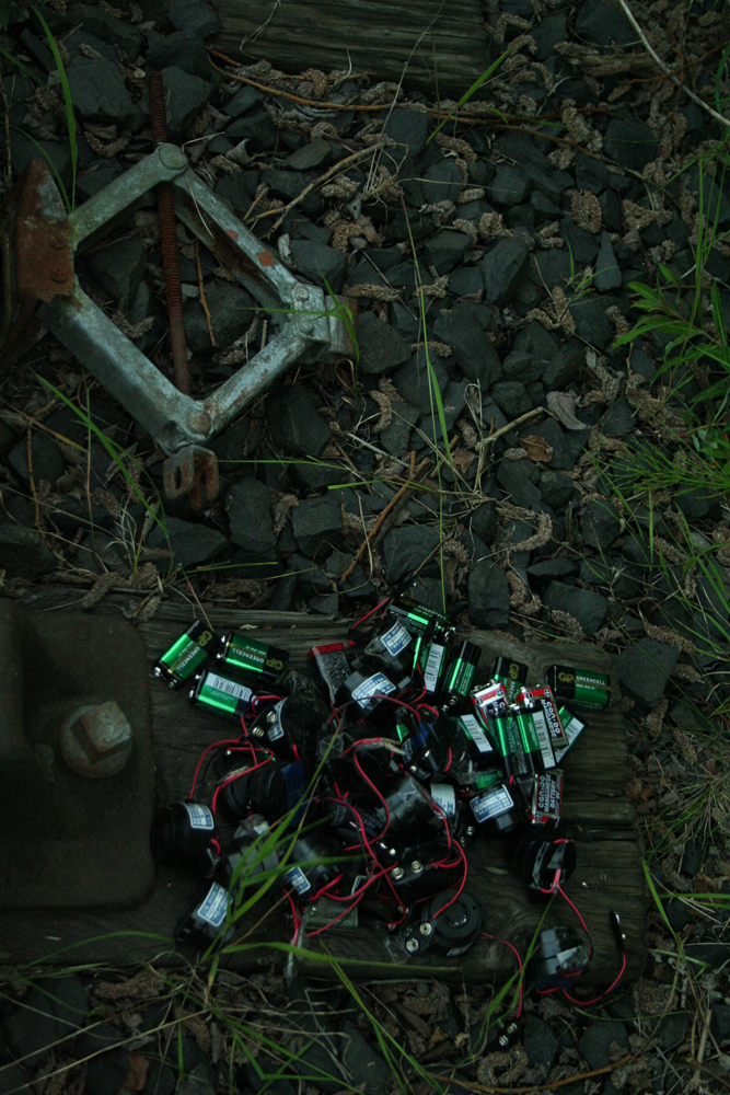 A bundle of batteries and electronic devices in a heap near track ballast