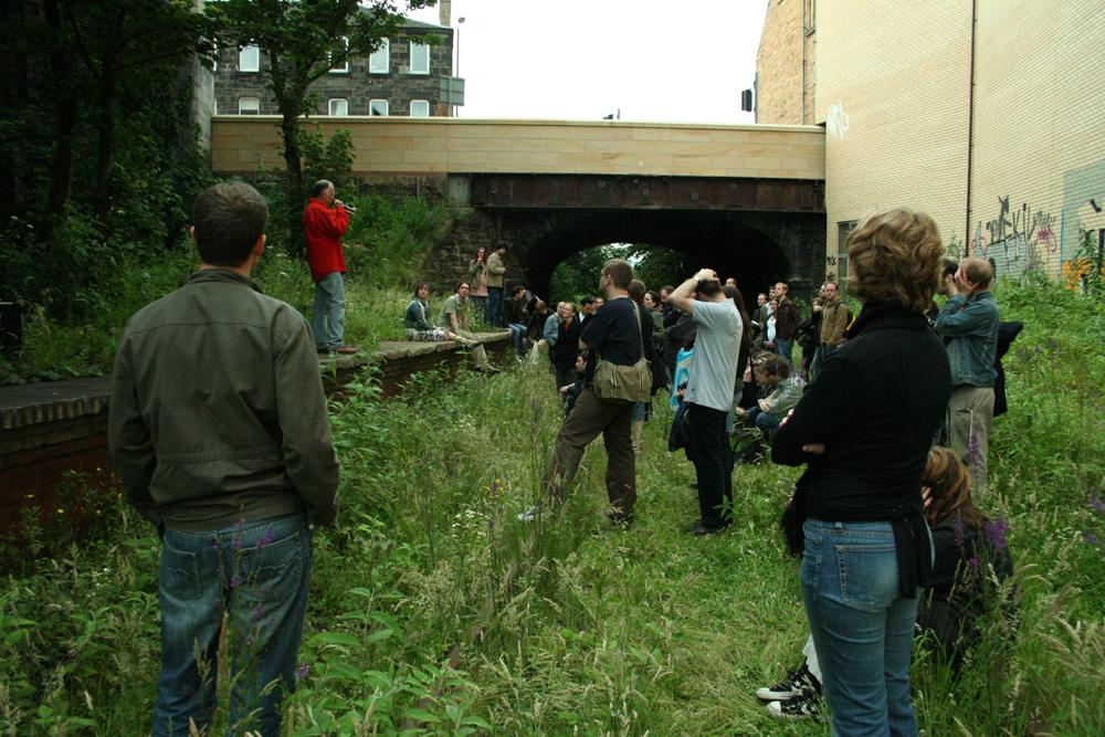 Denis Wood talking to an audience from an old railway platform