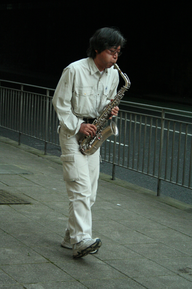 Tamio Shiraishi playing saxophone next to a fence in Edinburgh