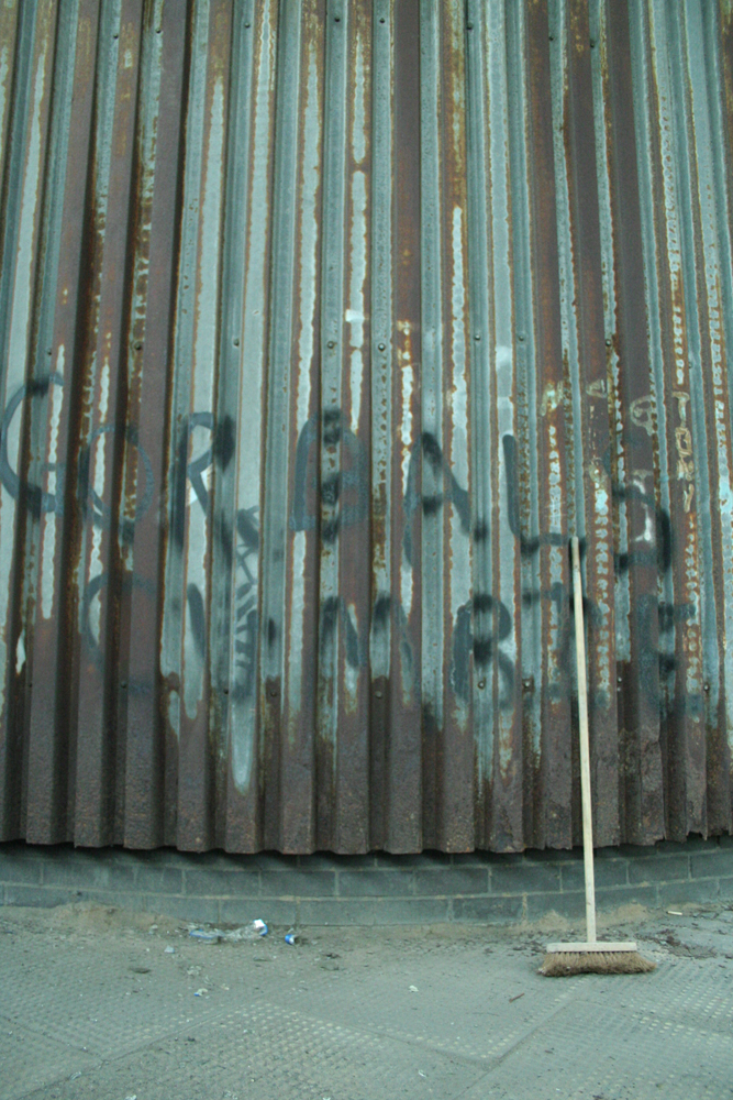 A corrugated iron wall with a brush against it