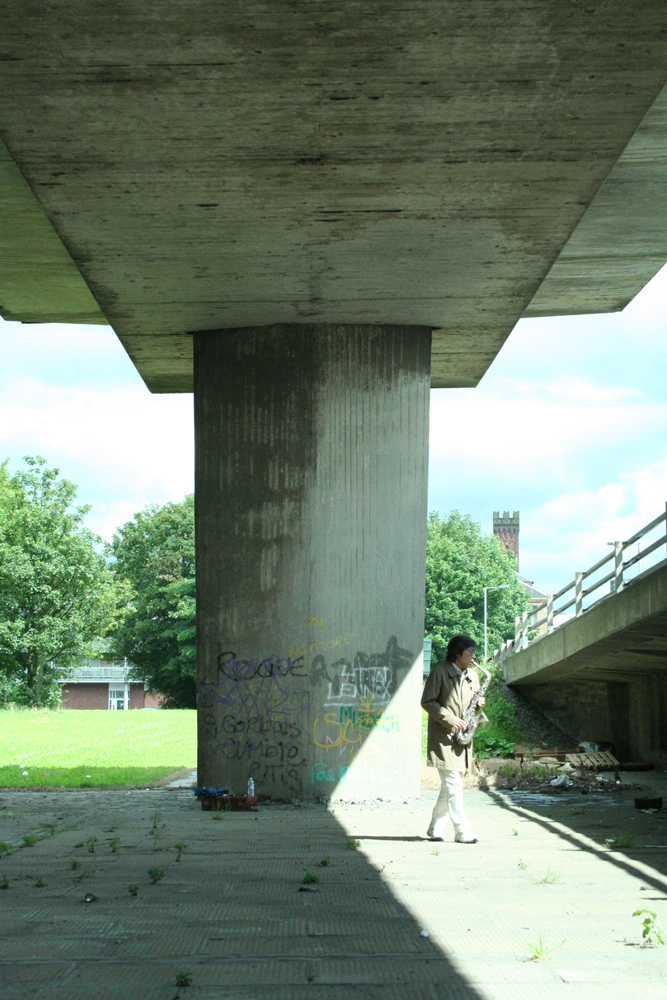Tamio playing saxophone beneath a concrete motorway structure