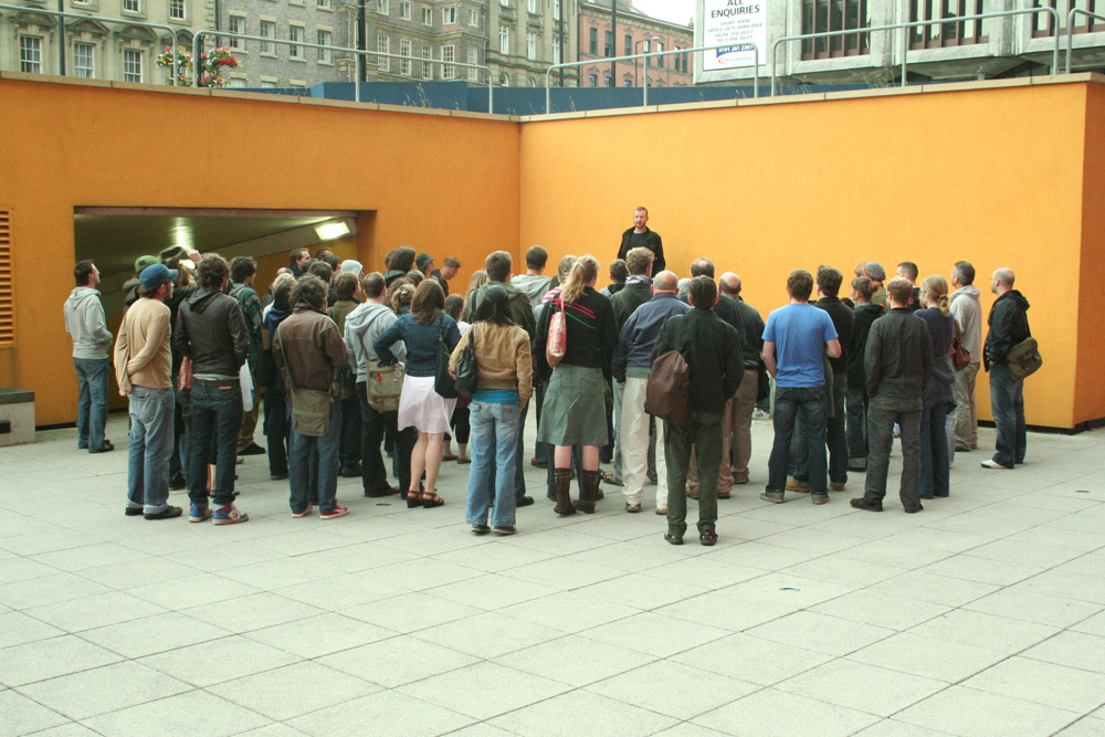 Audience assembled around a speaker near an orange wall in Newcastle