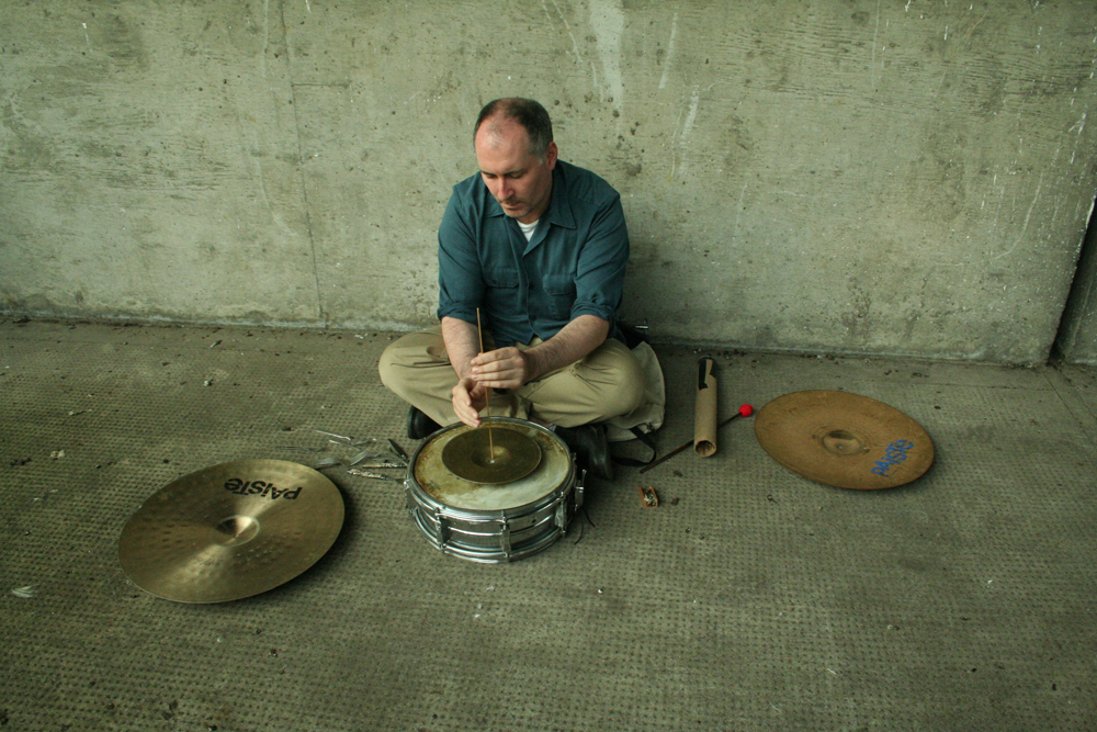 Sean meehan playing percussion on the ground in a concrete corner