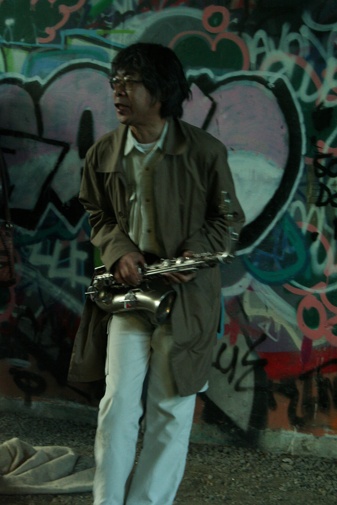 Tamio Shiraishi with saxophone against graffiti covered walls, white jeans