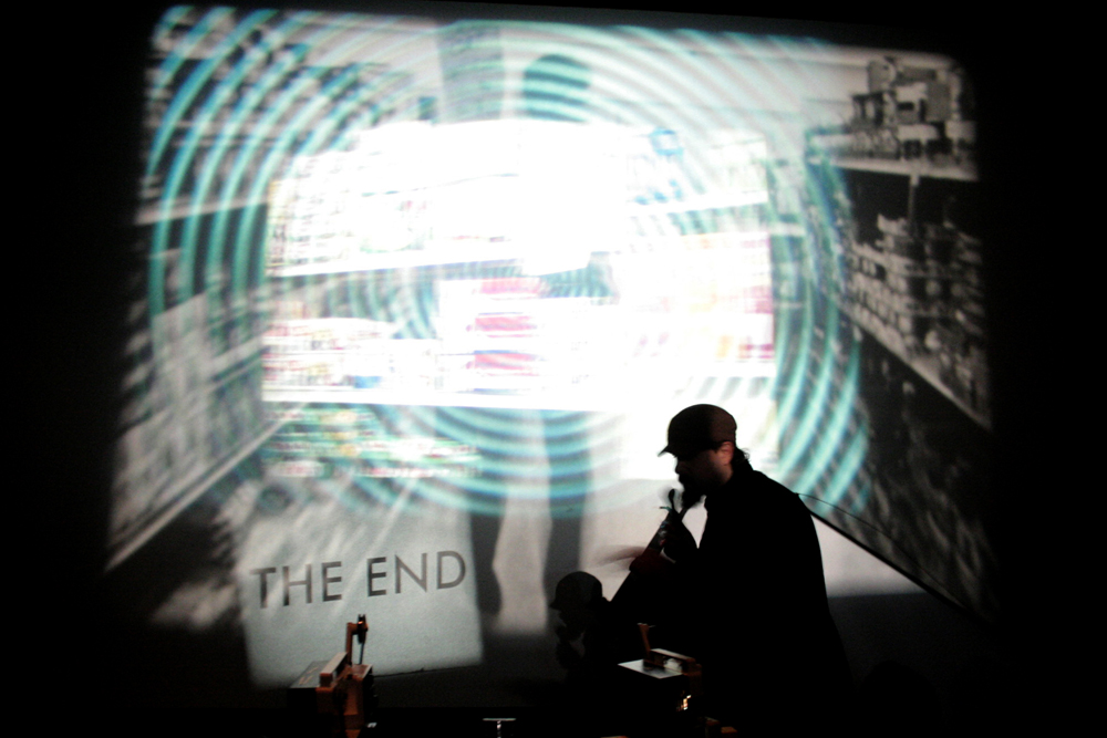 A man in front of a multi layered projection, a sign saying 'the end' 