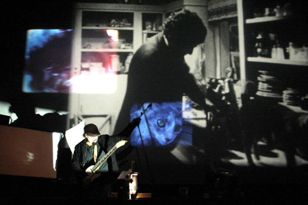 Andrew Lampert in front of projections playing a guitar