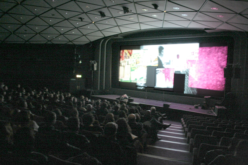 wide angle shot of theatre space with audience and many screens
