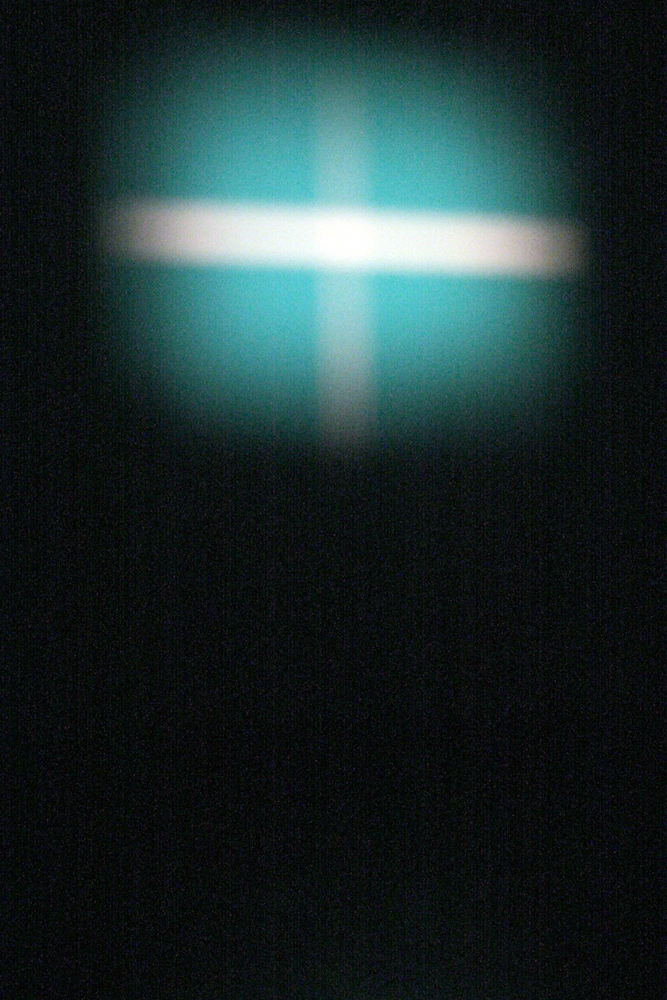A white cross over a chalky blue form is projected on a screen