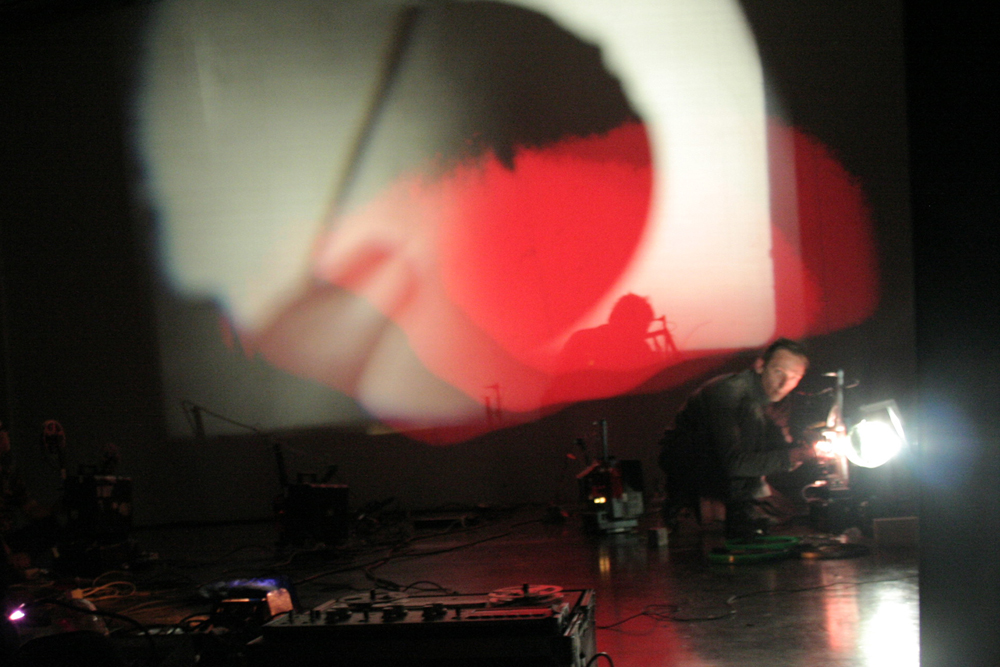 Large white and red forms projected near a man operating another projector